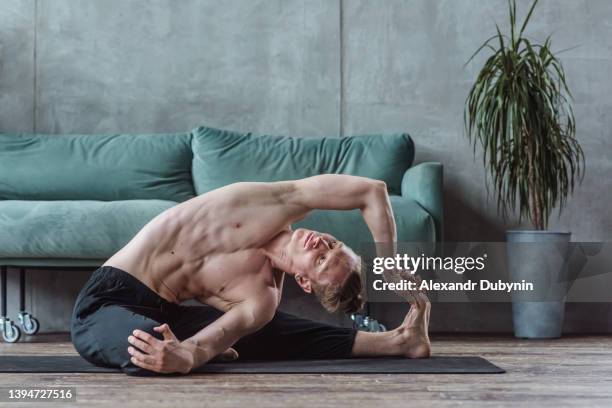 flexible man practices yoga in the morning at home in the living room on a mat. stretching exercise - man doing yoga in the morning photos et images de collection