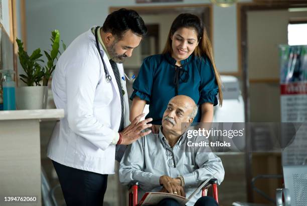 doctor consoling disabled man on wheelchair with daughter by his side at the hospital - family hospital old stockfoto's en -beelden