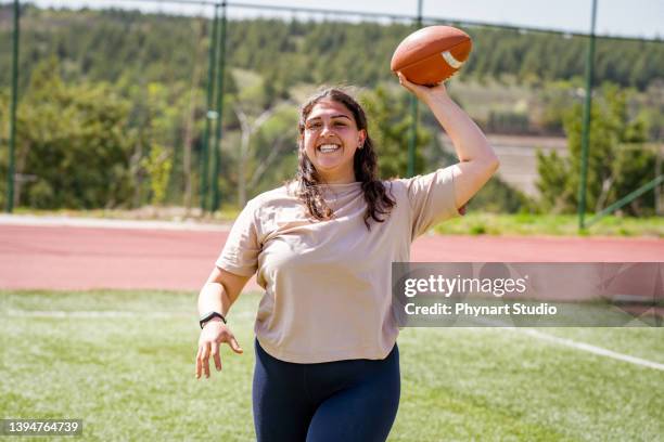 portrait of a young woman holding a football on a field - fat soccer players stock pictures, royalty-free photos & images