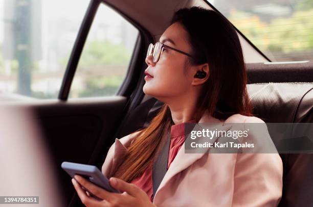 a southeast asian woman in smart casual clothing is using her smart phone while in a backseat of a car - daily life in philippines stock pictures, royalty-free photos & images