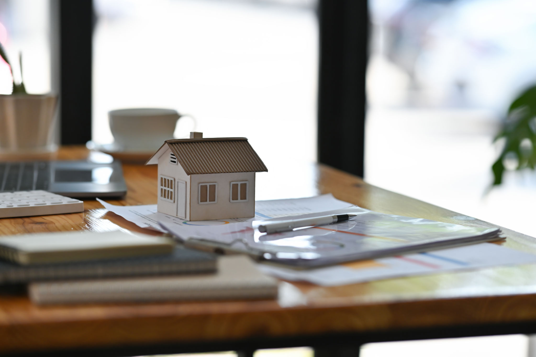 Cropped view of a house model placing on a paperwork on the table in the office for real estate business and finance concept. Cropped view of a house model placing on a paperwork on the table in the office for real estate business and finance concept.