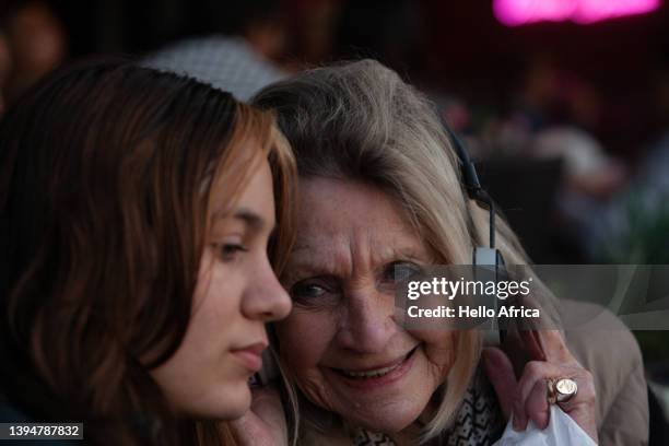 a fun grandmother listens to headphones with her granddaughter, with delight clearly visible on grandma's face - coole oma stock-fotos und bilder