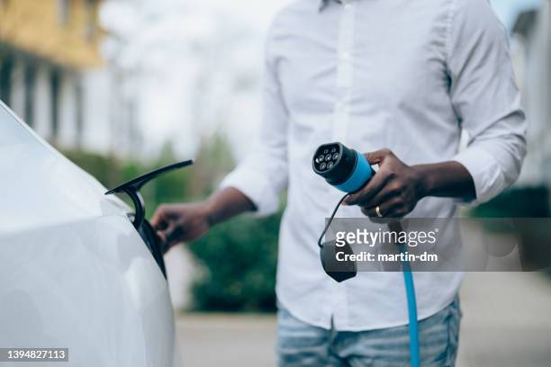 man charging electric car - electric car charging stock pictures, royalty-free photos & images