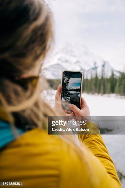 over the shoulder perspective of a woman taking a photo with a smartphone in the canadian rocky mountains - over the shoulder view stock-fotos und bilder