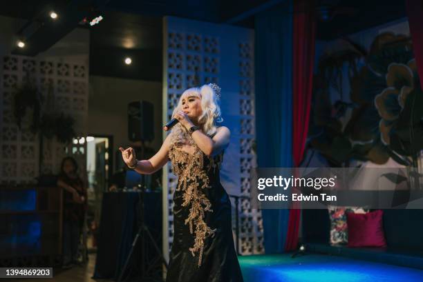 asian drag queen in spot lit stage performance at pub with audience in silhouette - comedian performing stock pictures, royalty-free photos & images