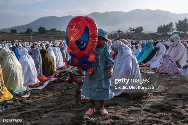 Girl holds balloon as Indonesian Muslims perform Eid Al-Fitr prayer on 'sea of sands' at Parangkusumo beach on May 02, 2022 in Yogyakarta, Indonesia....