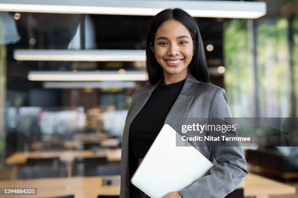 smart people with technologies to boost business success. portrait of confident young female entrepreneur standing while holding a laptop in a modern business office. - インドネシア人 ストックフォトと画像