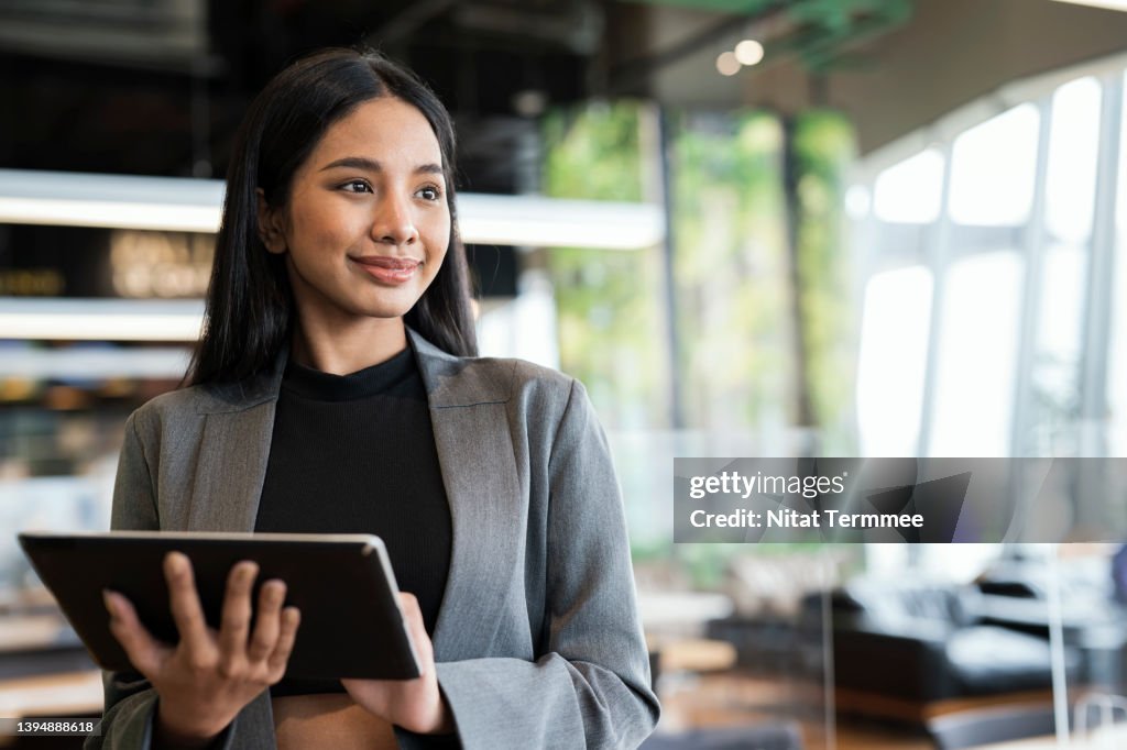 Empowering Women Business Entrepreneurs through Information and Communications Technology Solution. Portrait of a Young Businesswomen using a tablet while standing and looking away in a financial business office.