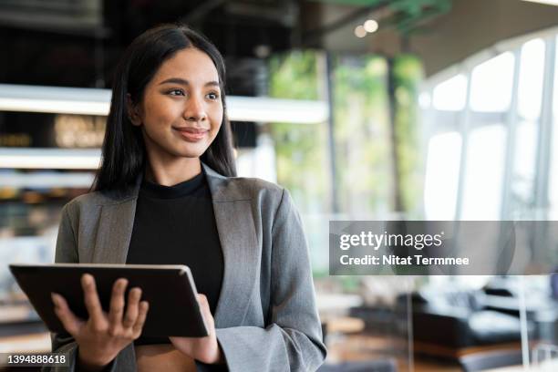 empowering women business entrepreneurs through information and communications technology solution. portrait of a young businesswomen using a tablet while standing and looking away in a financial business office. - aziatische etniciteit stockfoto's en -beelden