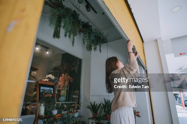 asian chinese female florist flower shop owner pushing up metal gate grill open for business - industrial doors stock pictures, royalty-free photos & images