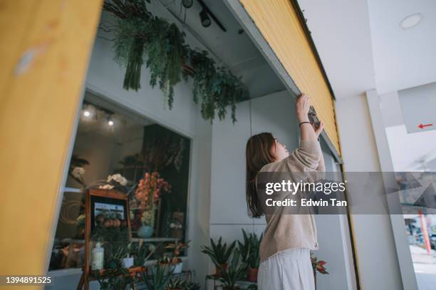 asian chinese female florist flower shop owner pushing up metal gate grill open for business - roller shutter 個照片及圖片檔