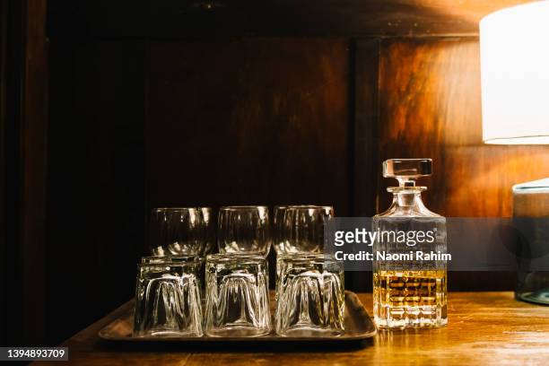 vintage-style whiskey decanter and glasses on a wooden bar counter, illuminated by a lamp - whisky bar stockfoto's en -beelden