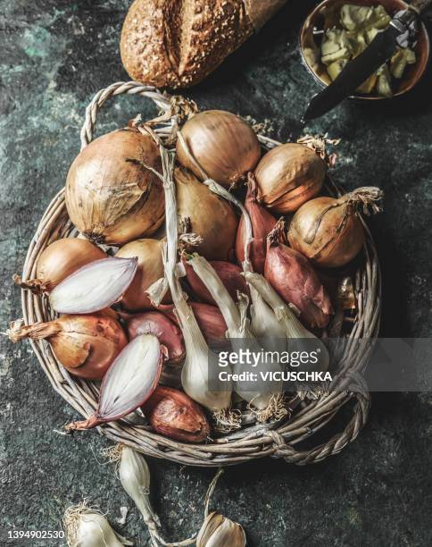 various onions in wooden basket at rustic kitchen table with bread and butter - onion soup stock pictures, royalty-free photos & images