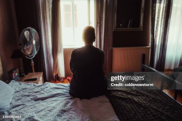 sad woman sitting alone on bed in hotel room - bedroom curtains stock pictures, royalty-free photos & images