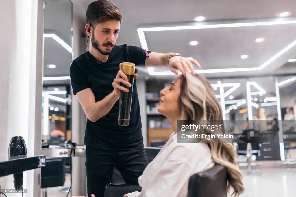 Hairdresser using hairspray at beauty salon