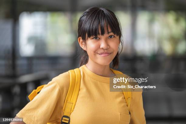 ritratto di giovane ragazza asiatica sobria che indossa una maglietta gialla e uno zaino in piedi a scuola all'aperto - 14 foto e immagini stock