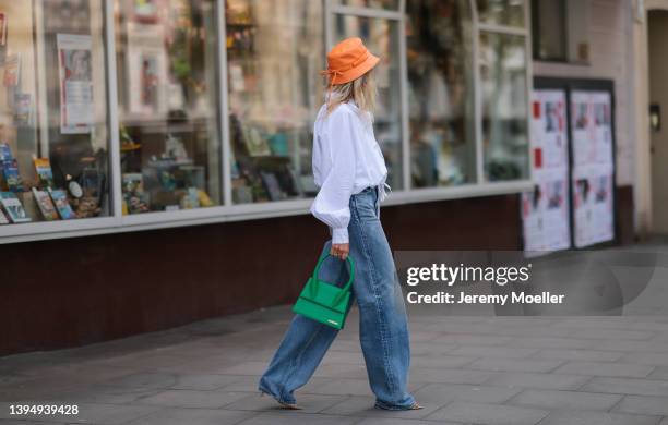 Sue Giers seen wearing an orange leather bucket hat from Jacquemus, a dark blue wide leg denim jeans from Celine, a white SoSue blouse shirt, a green...