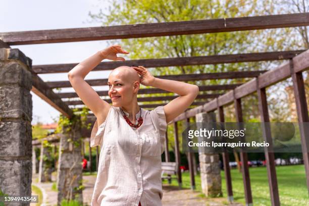 a bald caucasian woman enjoying life after surviving breast cancer in a park in spring, smiling and very happy with her arms up - woman smiling eyes closed stock pictures, royalty-free photos & images