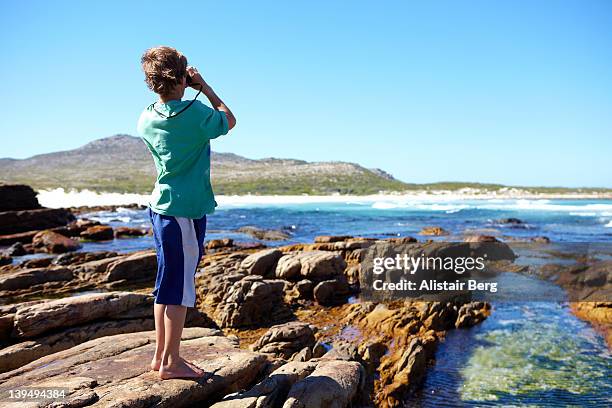 boy looking through binoculars by the sea - boy exploring on beach stock pictures, royalty-free photos & images