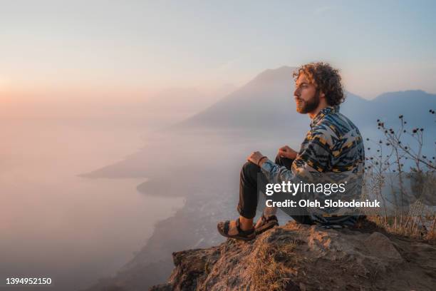 man sitting on mountain on  the background of atitlan lake in guatemala at sunset - looking above stockfoto's en -beelden