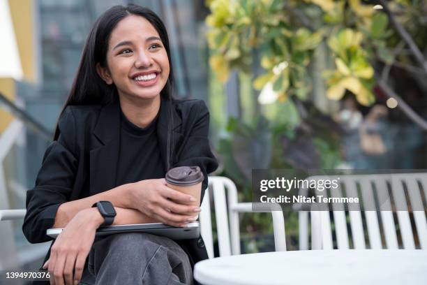 inspiring young entrepreneurship through creative thinking for startup new business. young businesswoman holding a laptop and coffee cup while taking a break at sidewalk coffee shop. - alleen één jonge vrouw stockfoto's en -beelden