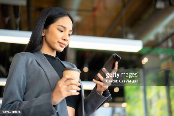 portrait of young asian businesswoman managing online banking with mobile app on smartphone on the go. transferring money, paying bills, checking balance in the coffee shop background. - frank rich stock pictures, royalty-free photos & images
