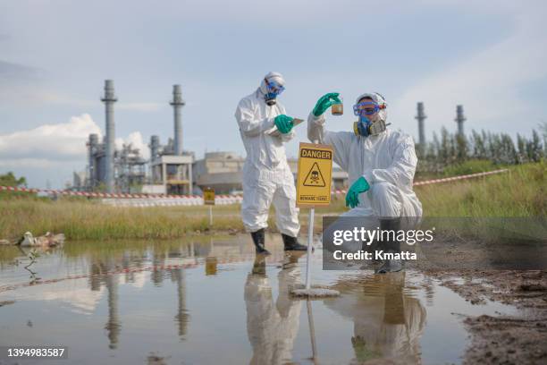 scientists in radiation protection suit examining polluted water at industrial site. - radioactive warning symbol photos et images de collection