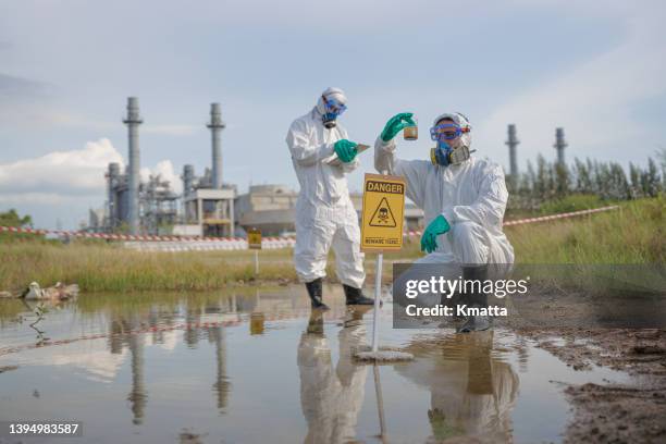scientists in radiation protection suit examining polluted water at industrial site. - segnale di pericolo di radiazioni foto e immagini stock