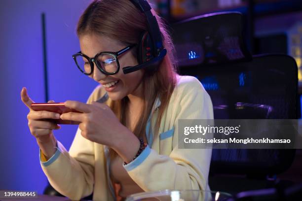 excited asian woman playing mobile game on smartphone in the evening at home. - mobile game stock pictures, royalty-free photos & images