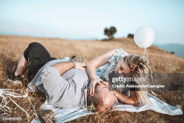 cute couple celebrating anniversary by lying down together on hill in nature with balloons - fat man lying down stock pictures, royalty-free photos & images