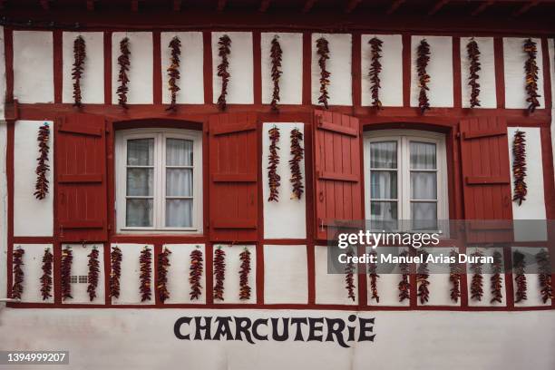 white facade with red wooden windows. on the facade there are hanging peppers drying. - france chili stock pictures, royalty-free photos & images