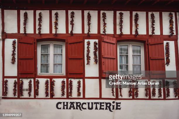 white facade with red wooden windows. on the facade there are hanging peppers drying. - espelette france imagens e fotografias de stock