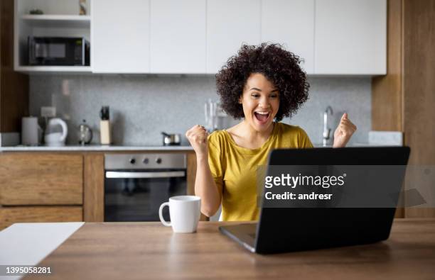 excited woman at home working on her laptop and winning something - excitement computer stock pictures, royalty-free photos & images