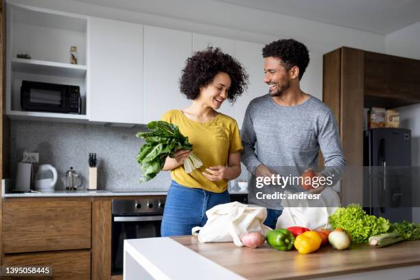happy couple unpacking the groceries after arriving home from the supermarket - young man groceries kitchen stockfoto's en -beelden