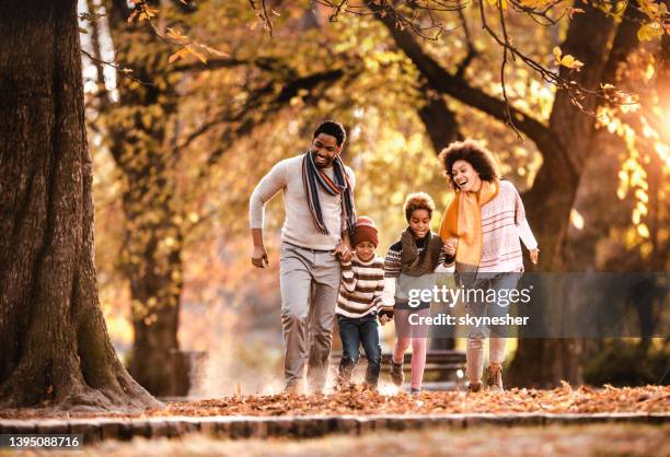 carefree black family holding hands and running in autumn at the park. - season stock pictures, royalty-free photos & images