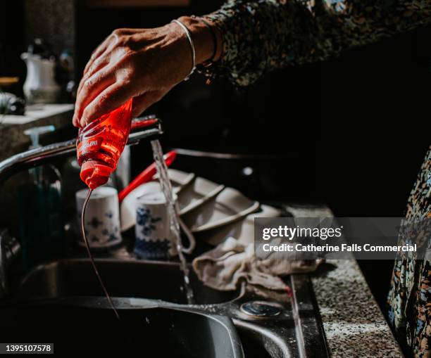 a hand squeezes washing up liquid into a sink - liquide vaisselle photos et images de collection