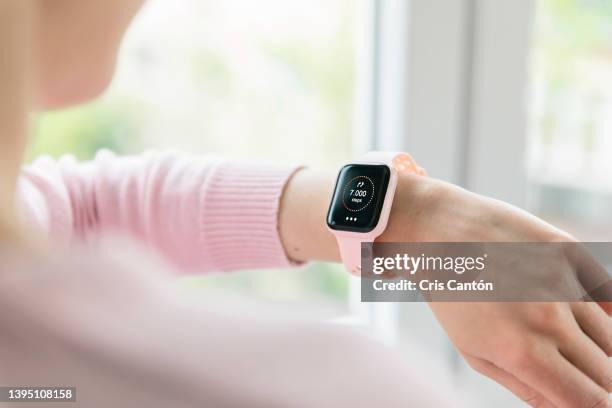 woman checking daily steps mockup on pink smartwatch at home - smartwatch stock-fotos und bilder