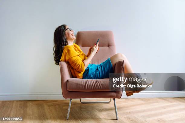 young laughing  female worker in casual outfit using phone and chilling out at free time - armchair stock pictures, royalty-free photos & images