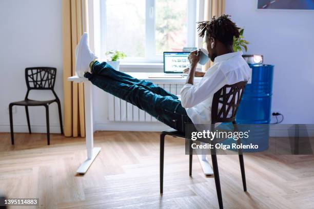 smiling and relaxing interracial man in white shirt in office, using laptop for social media and shopping online, lazy atmosphere - back of office chair stock pictures, royalty-free photos & images