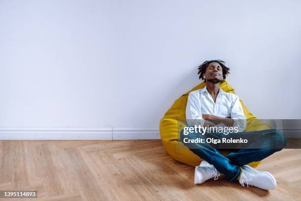 young man with dark dreadlocks relaxing in a beanbag chair, listening to music, create new ideas. - bean bags fotografías e imágenes de stock