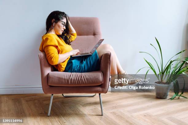 young female worker in casual outfit using laptop  for work in lounge room - femme assise bureau photos et images de collection
