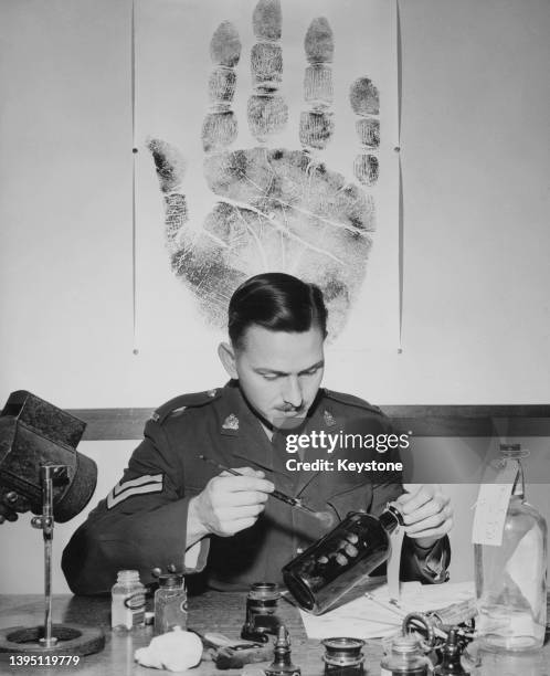Corporal JHSP Jones, in charge of the Royal Canadian Mounted Police Criminal Investigation Branch examines a bottle - evidence in a police...