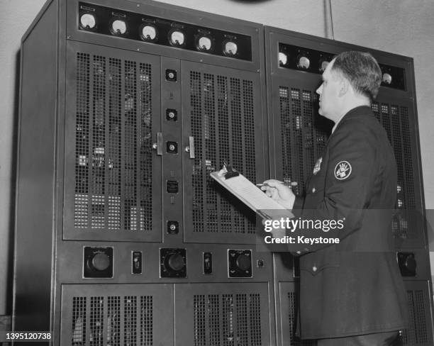 An NYPD officer inspects Western Electric radio equipment housed within a cabinet, with dials and gauges on the front, at police headquarters in New...