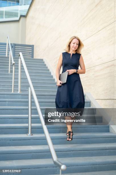 elder business woman with laptop walking on stairs outside office building in the city - old emirati woman stock-fotos und bilder