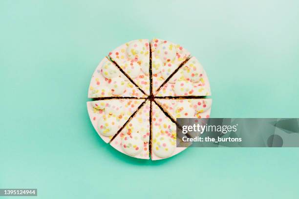 high angle view of a cream cake divided into equal parts on turquoise background - birthday cake overhead stock pictures, royalty-free photos & images