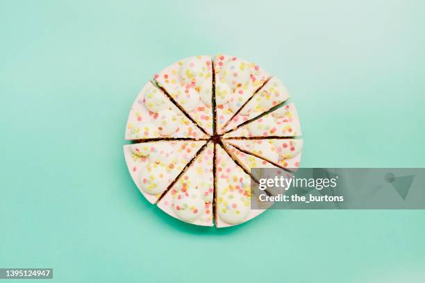 high angle view of cream cake divided into pieces of different sizes on turquoise background - teilabschnitt stock-fotos und bilder