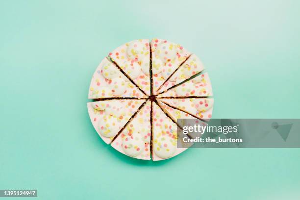 high angle view of cream cake divided into pieces of different sizes on turquoise background - pie chart food stock pictures, royalty-free photos & images