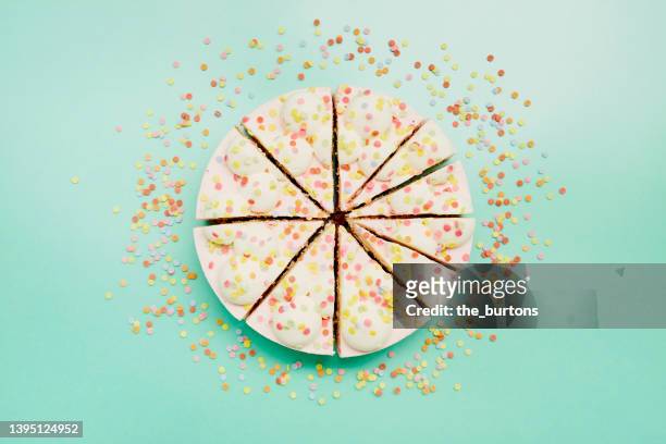 high angle view of cream cake divided into pieces of different sizes on turquoise background - birthday cake overhead stock pictures, royalty-free photos & images