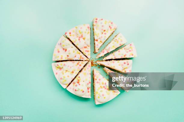 high angle view of cream cake divided into pieces of different sizes on turquoise background - taartpunt stockfoto's en -beelden