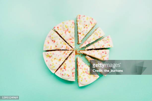 high angle view of cream cake divided into pieces of different sizes on turquoise background - fatia de bolo - fotografias e filmes do acervo